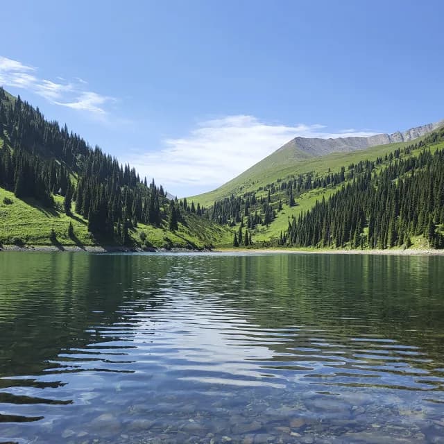 Clear glacial water of the Second Kolsay Lake (Minzhylgy) surrounded by dark forest